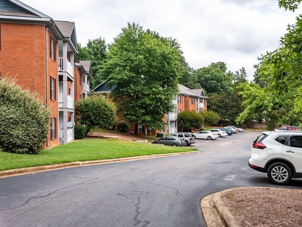 Parking lot beside brick apartment buildings with trees and greenery.