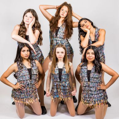 A group of six young female dancers in shiny costumes posing.