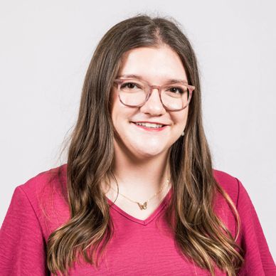 Smiling woman with glasses and long hair wearing a pink top.