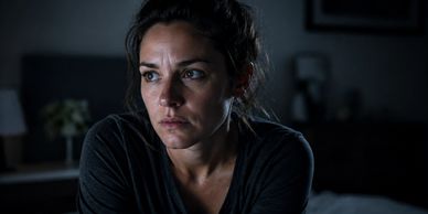 A woman looks worried and thoughtful in a dimly lit room.