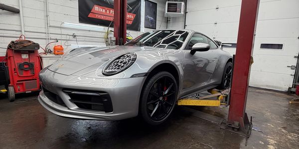 Silver sports car on a lift in an auto repair shop.