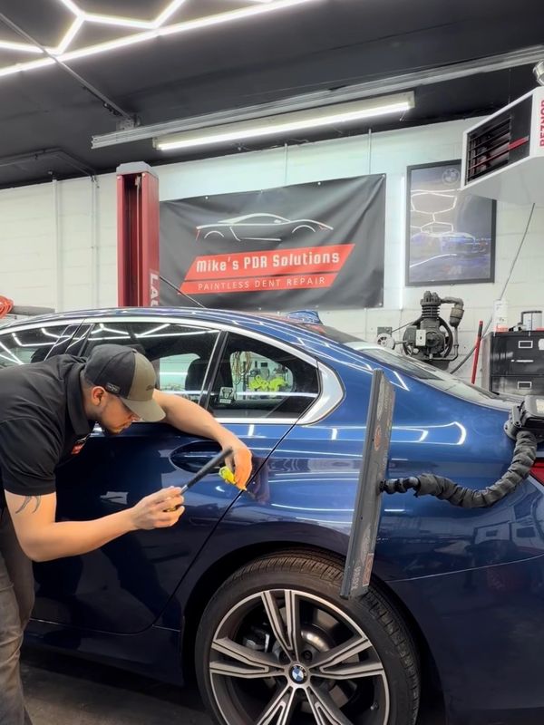 Technician repairing a dent on a blue BMW using paintless dent repair tools.