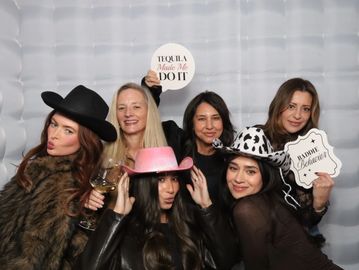Six women posing with cowboy hats and fun signs in a photo booth.