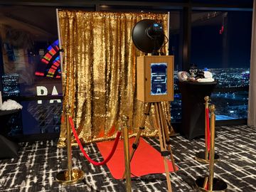 A gold sequin photo booth setup with red carpet and city night view.