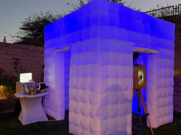Inflatable photo booth glowing blue at dusk in a backyard.