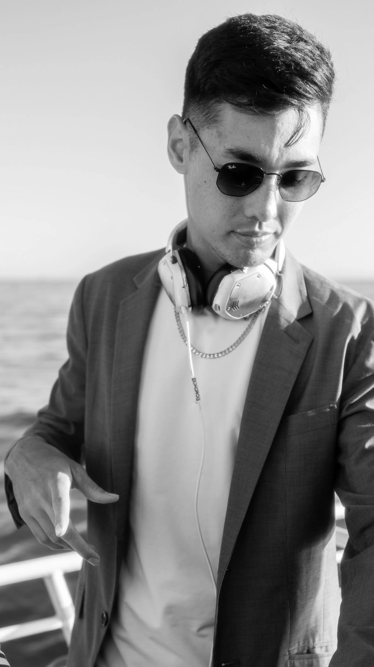 Man in sunglasses with headphones around his neck, dressed in a blazer.