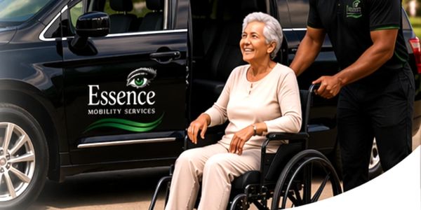 A smiling elderly woman in a wheelchair being assisted by a caregiver near Essence Mobility Services vehicle.
