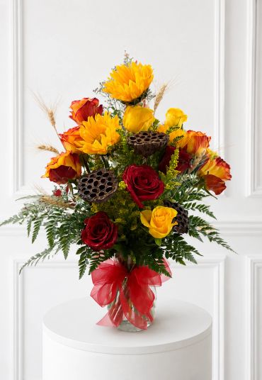 Bright floral arrangement with roses and sunflowers tied with a red ribbon.