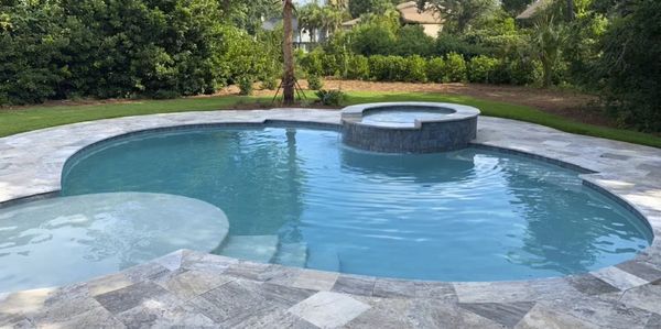 A clear blue backyard pool with an elevated spa surrounded by stone tiles.
