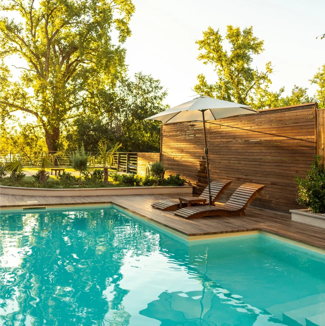 Sunny backyard pool with wooden lounge chairs and a large umbrella.