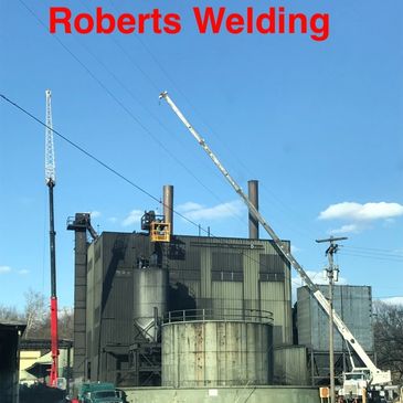 Industrial building with cranes and welding work under clear blue sky.
