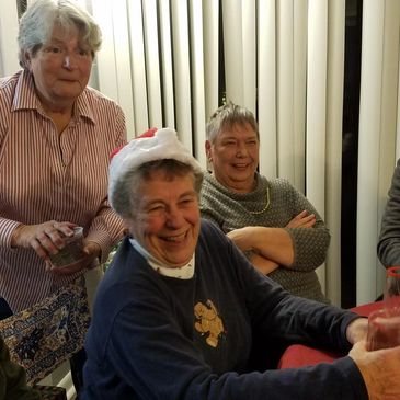 Three elderly women enjoying a gathering, one wearing a Santa hat.