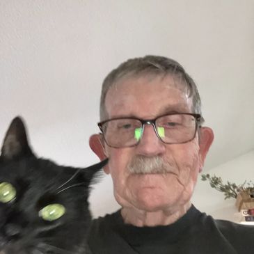 Selfie of an older man with glasses and a black cat.