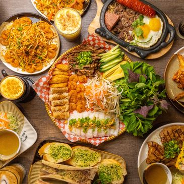 A vibrant spread of Vietnamese dishes featuring grilled meats, shrimp, fresh herbs, and various sides.