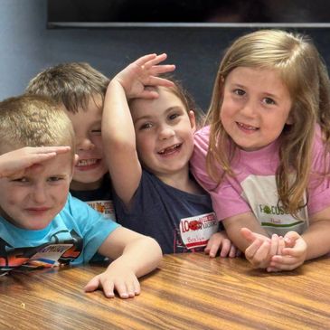 Four kids smiling and posing at a table.