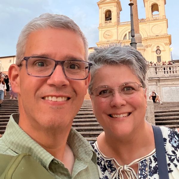 Smiling couple taking a selfie on stairs in front of historic building.