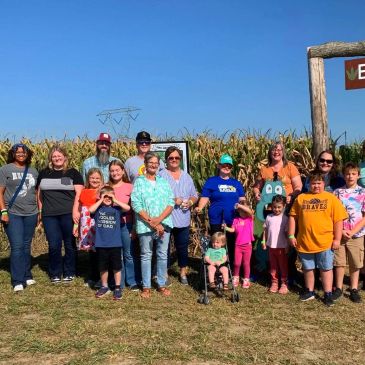 Group of people posing in front of a cornfield under a clear blue sky.