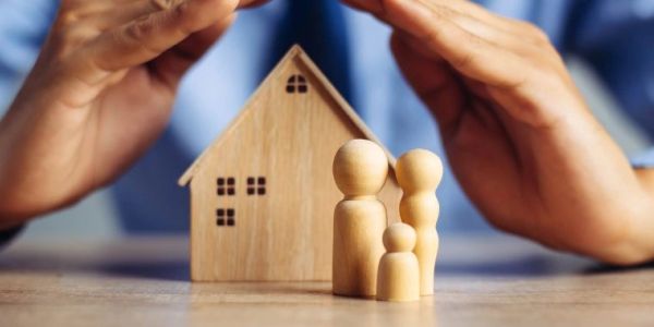 Hands protecting a wooden house and family figures.