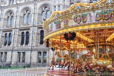 A bright carousel is lit up in front of the Natural History Museum.