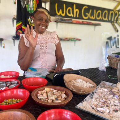 Smiling woman waves at camera behind table of local nuts and shells.