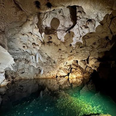 Inside a limestone cave with reflective water and rugged ceiling formations.
