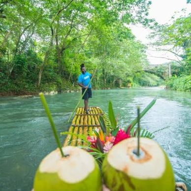 A person steers a bamboo raft on a river surrounded by lush greenery.