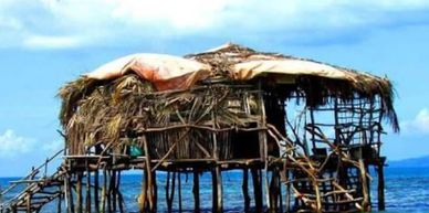 A rustic hut on stilts over water under a blue sky.