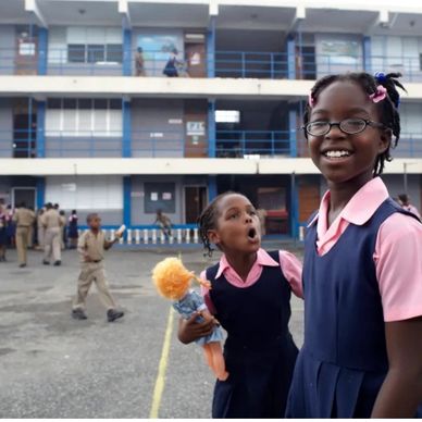 Two smiling schoolgirls in uniform at a school playground.