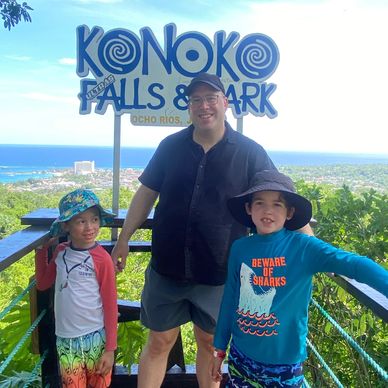 A man and two boys posing at Konoko Falls &amp; Park with a scenic ocean view.