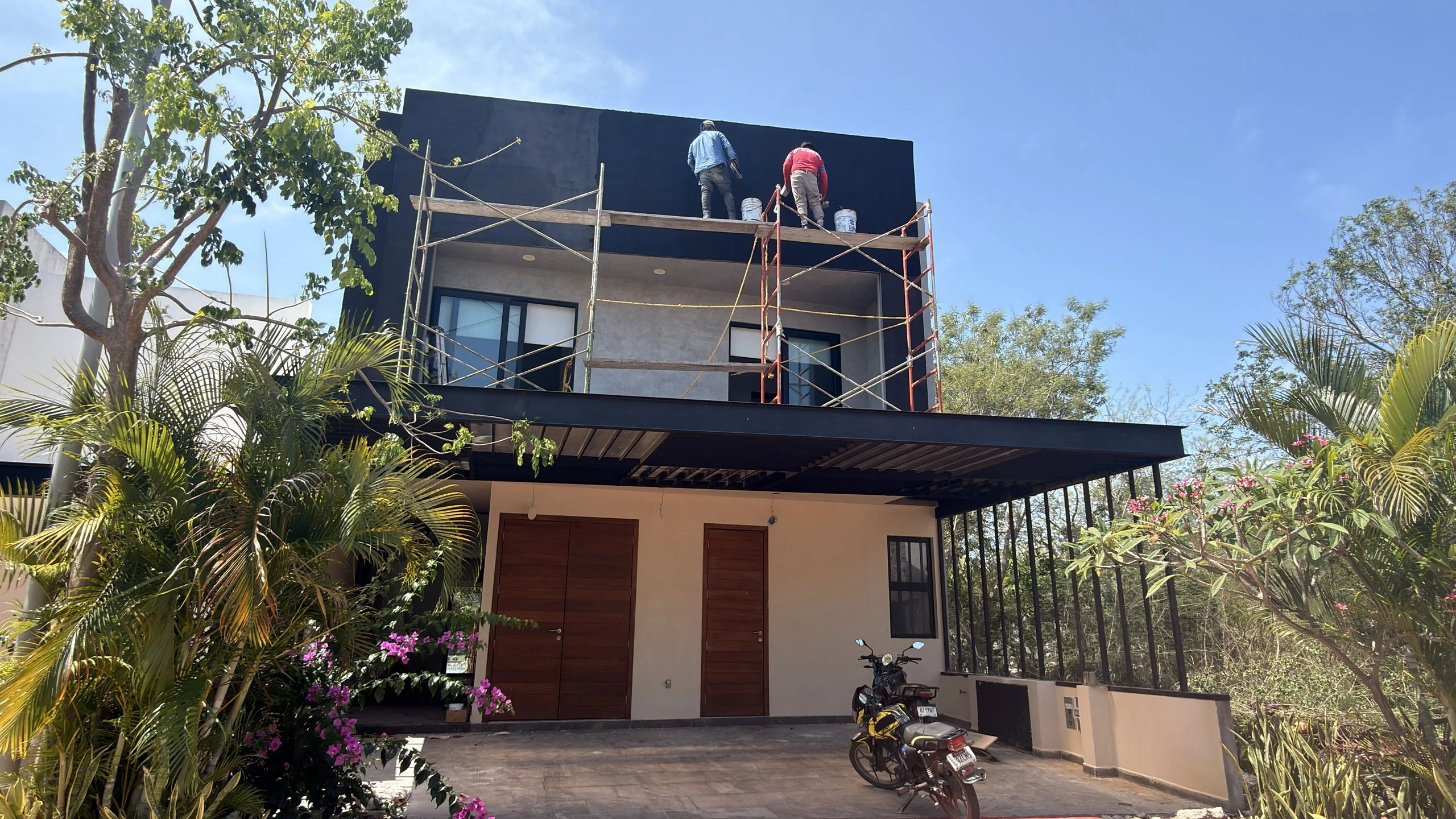 Dos personas pintando la parte superior de una casa moderna en un día soleado.