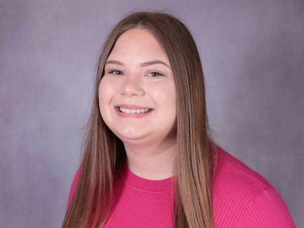 Young woman with long hair smiling in a pink top.
