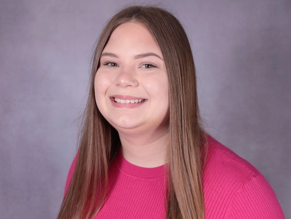 Young woman with long hair smiling in a pink top.
