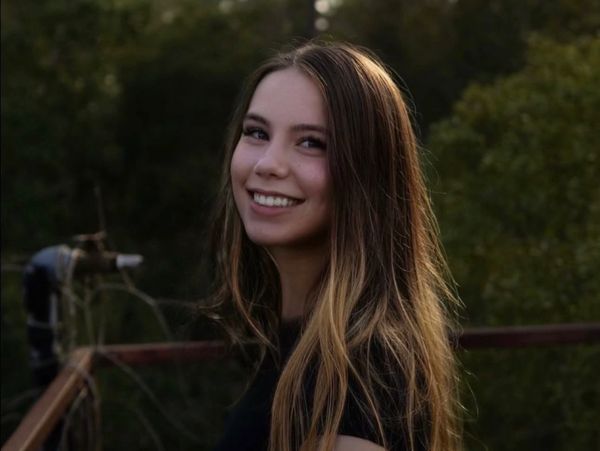 Young woman with long hair smiling outdoors.