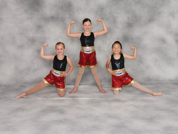 Three girls in matching dance outfits flexing muscles.