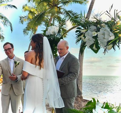 A couple smiles towards the guests while their good friend reads from a binder and officiates.