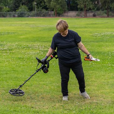 Person using a metal detector on a grassy field.