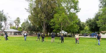 People spread out in a park holding metal detectors on grassy field.