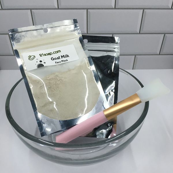 Goat milk face mask powder and brush in a glass bowl on a tiled counter.