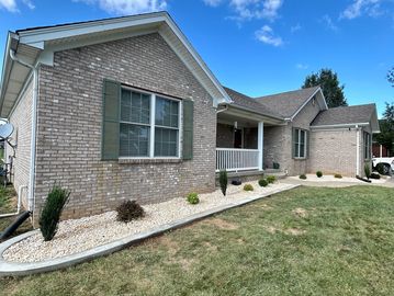 Single-story brick house with green shutters and a landscaped front yard.