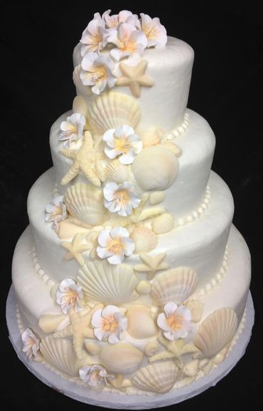 A four-tier white cake decorated with seashells, starfish, and white flowers.