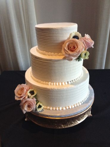 Elegant three-tiered white wedding cake adorned with soft pink and white flowers.