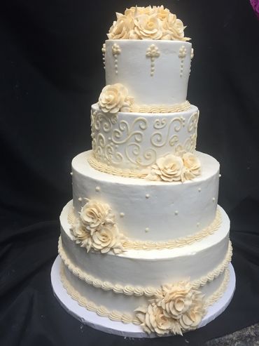 Elegant four-tier white cake decorated with cream flowers and intricate piping.
