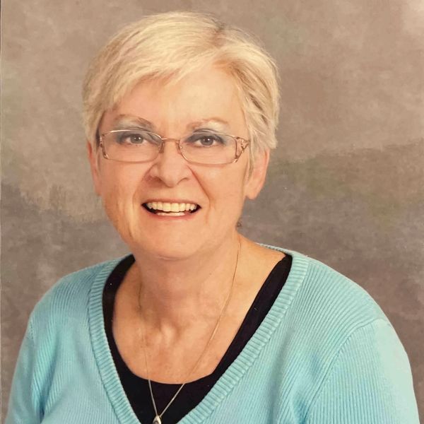 Smiling elderly woman with glasses wearing a light blue sweater.