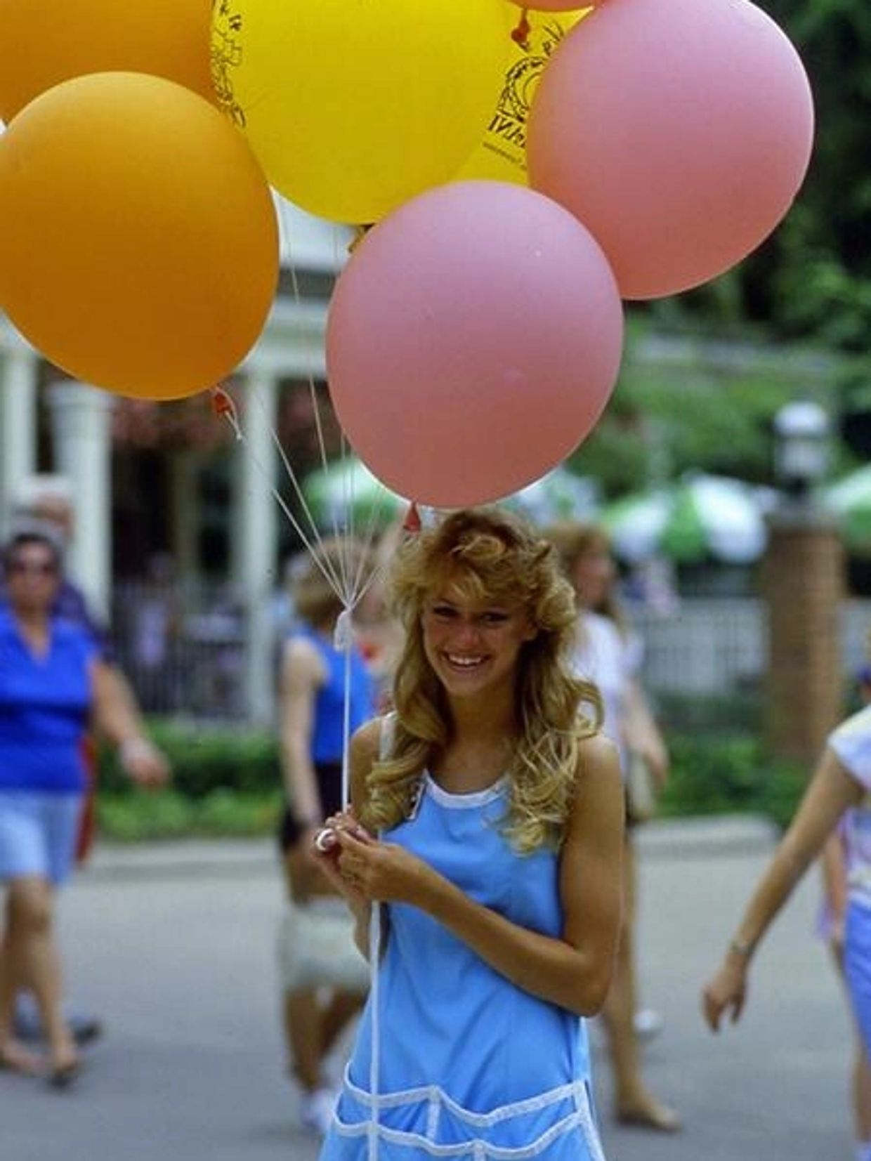 Smiling woman in blue dress holding colorful balloons outdoors.