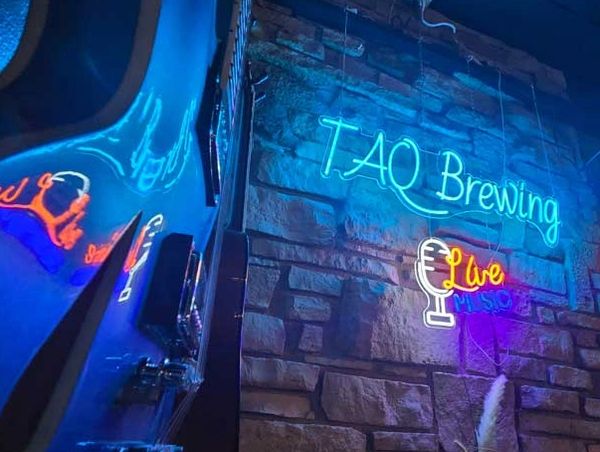a blue guitar next to a neon sign that says " TAQ Brewing Live Music "