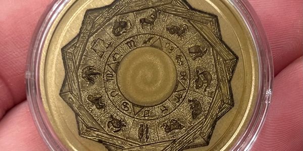 A gold coin featuring the zodiac signs in a clear protective case.