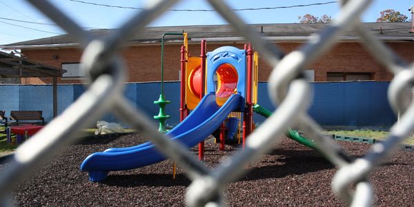 Playground with a blue slide seen through a chain-link fence.