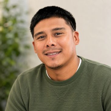 A smiling man in a green sweater posing outdoors.