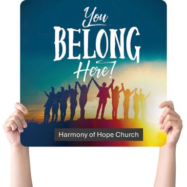 Hands hold sign saying 'You Belong Here!' with silhouettes of people celebrating.