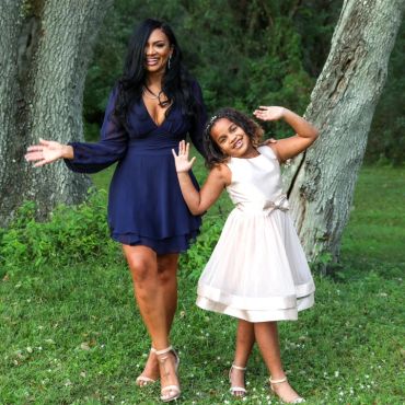 Woman and girl smiling outdoors in dresses.